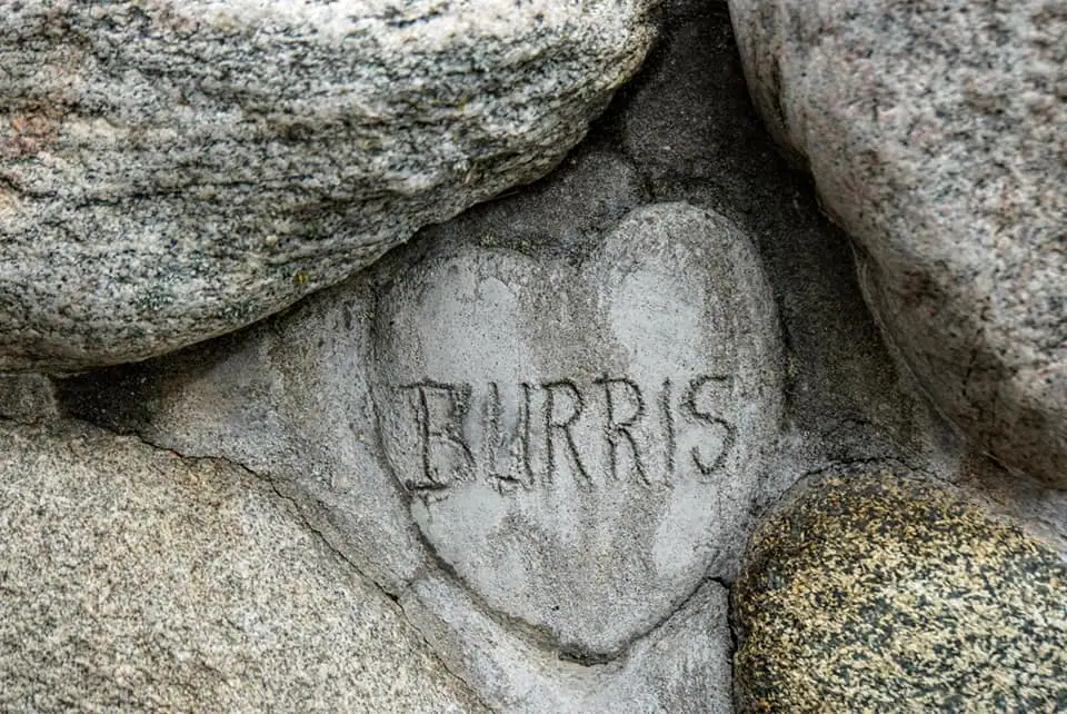 Close-up of the name “BURRIS” carved into a pale stone among larger rocks.