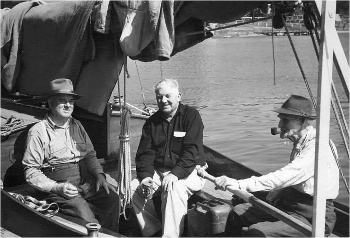 Three men sit aboard a rigged boat beside calm water, with ropes, canvas, and a smoking pipe visible.