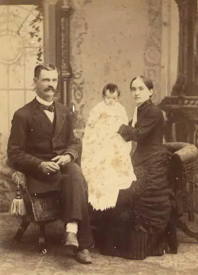 Sepia studio portrait of a seated man and woman with a baby between them.