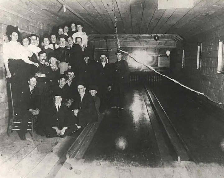 A group of adults poses beside polished bowling lanes in a wooden interior.