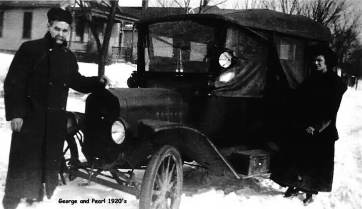 Two adults pose beside an antique automobile in snow, with a caption identifying them and the era.