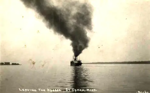 A small steamship moves across calm water, trailing a large plume of dark smoke.
