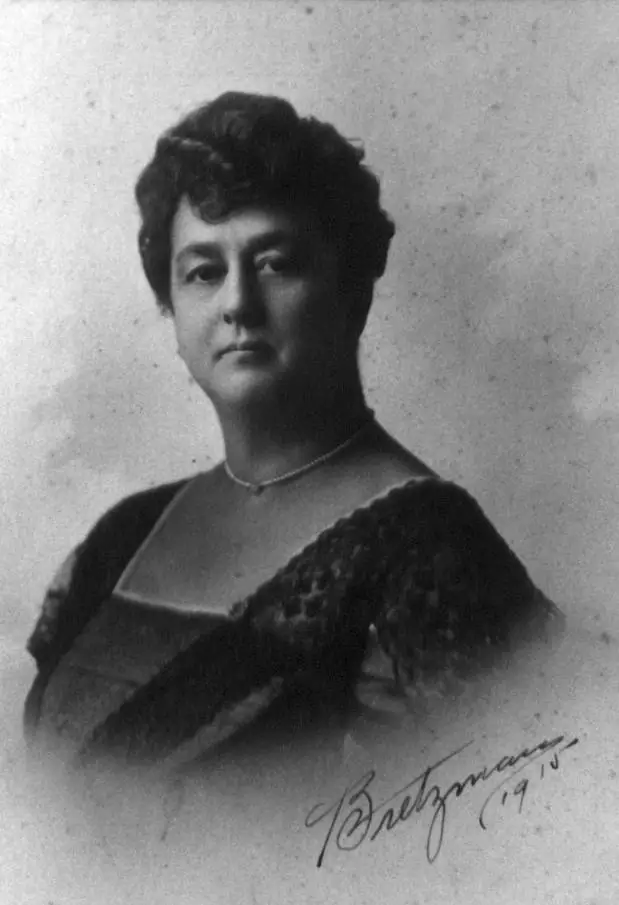 Black-and-white studio portrait of a woman in a dark dress with a lace-trimmed neckline and necklace.