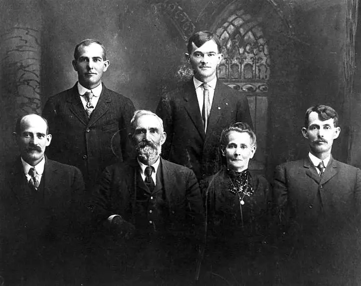 Black-and-white formal portrait of six people posed in two rows before an ornate backdrop.