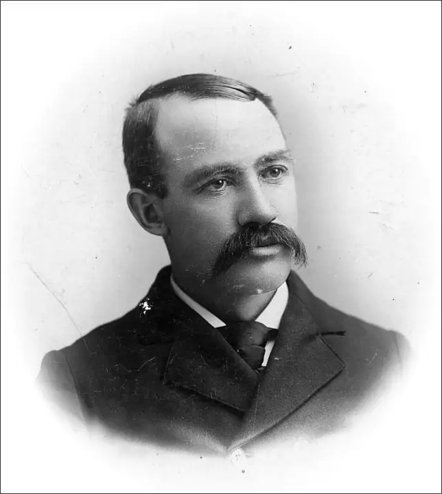 Black-and-white studio portrait of a mustached man in a suit and tie.