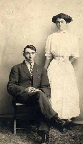 Studio portrait of a seated man and standing woman in formal clothing.
