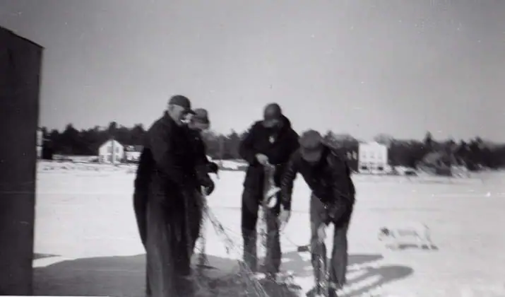 Four bundled men pull a fishing net across a snow-covered frozen surface.