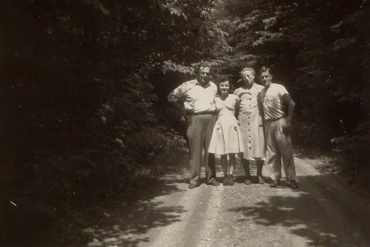 Four people pose on a sun-dappled dirt path surrounded by dense trees.