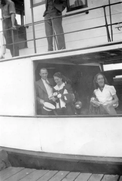 Three people stand in a ship’s open side while two more are partly visible on the deck above.