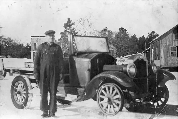 A person stands beside a vintage automobile in a snowy outdoor setting.