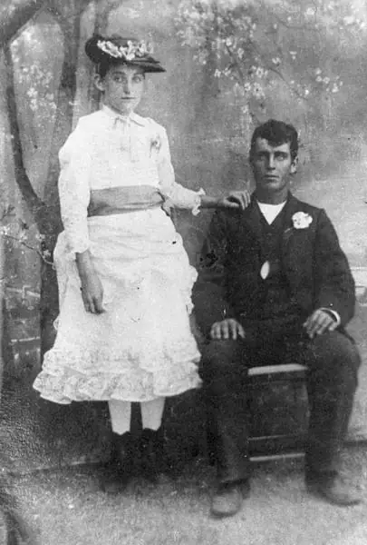 Black-and-white formal portrait of a woman standing beside a seated man in a studio setting.