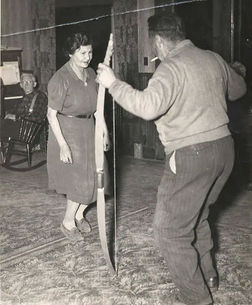 Three people in a room, with a man holding a long narrow object beside a woman.