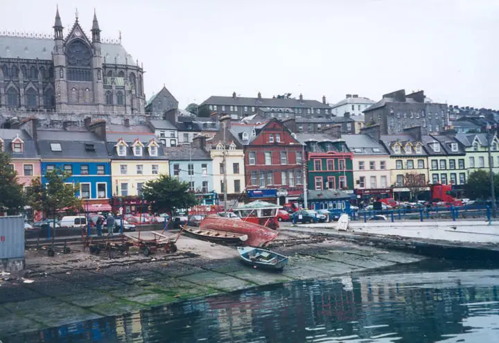 A waterfront town with colorful row houses, small boats, and a large Gothic church rising behind them.