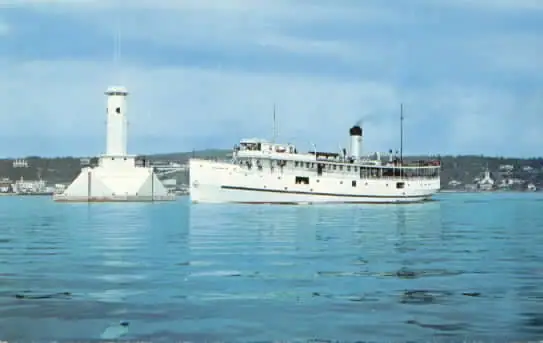 White passenger ferry beside a cylindrical lighthouse on a concrete pier.