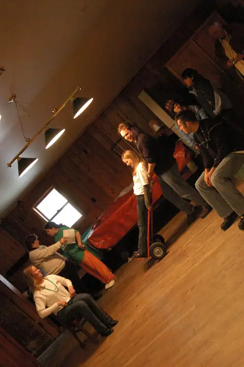A group gathers in a wood-paneled room around a red wheeled object.