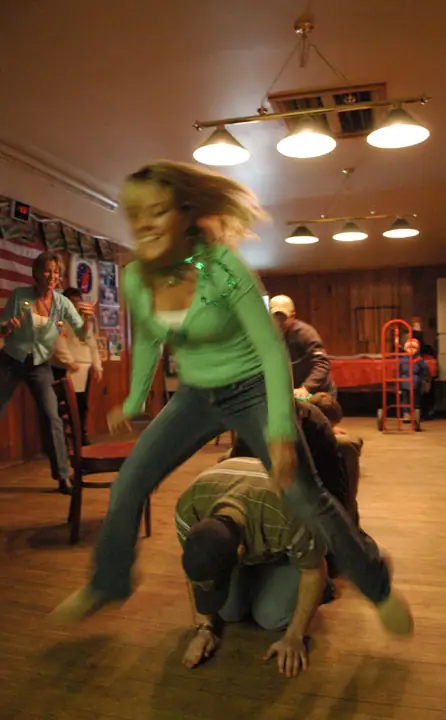 A woman steps over a person on the floor as others gather in a wood-paneled room.