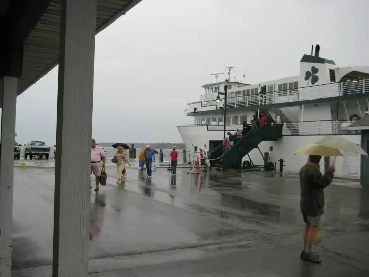 A white ferry is boarded in the rain as people cross a wet dock with umbrellas.