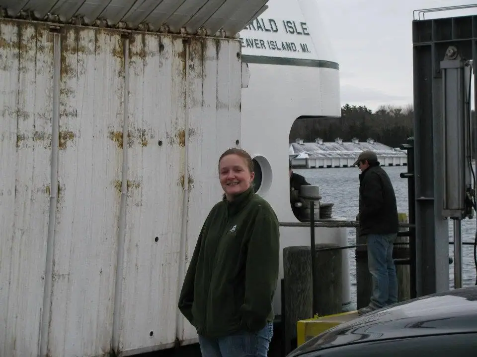 Two people stand on a ferry deck beside a weathered white superstructure marked with partial lettering.