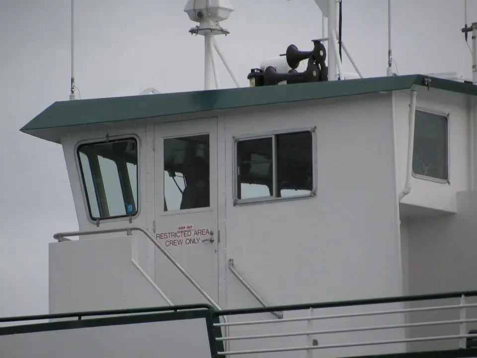 White vessel bridge with green roof, deck railings, navigation equipment, and a restricted-area door.