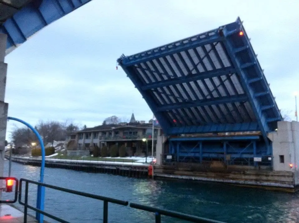 A blue drawbridge stands raised above a waterway beside a multistory building in winter.