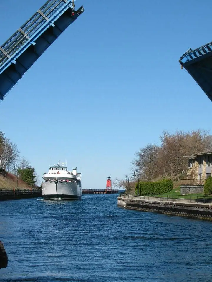 A passenger ferry approaches beneath a raised drawbridge, with a red lighthouse visible beyond the waterway.