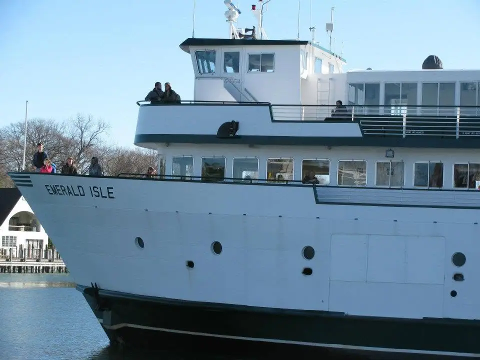 Large white ferry with dark hull docked beside a pier, with people visible on its decks.