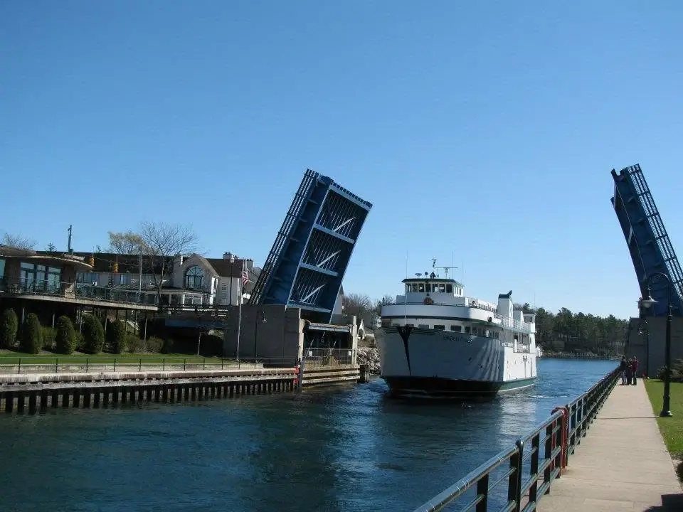 A white passenger ferry passes between the raised leaves of a blue drawbridge.