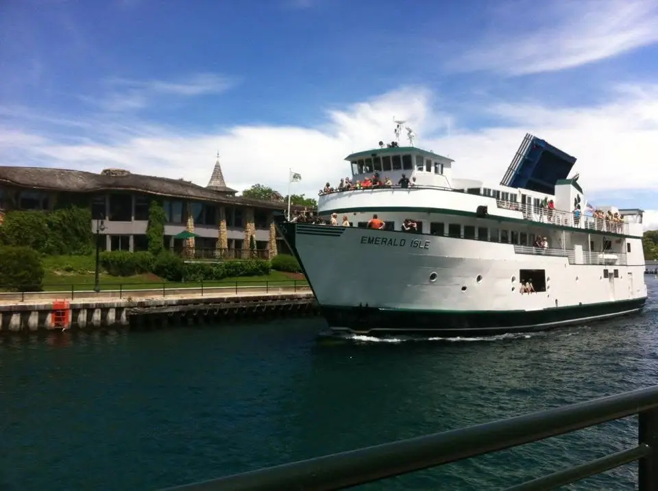 A white passenger ferry passes a waterfront building and pier, with people visible on its decks.