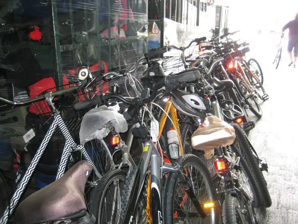 Several bicycles are parked closely together in front of a reflective storefront window.