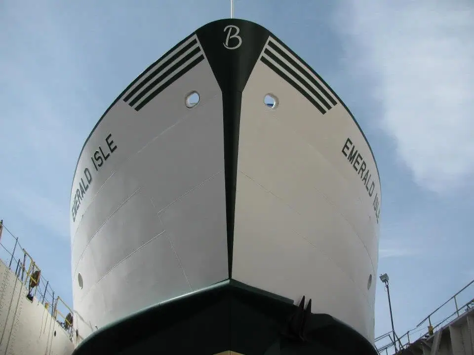 Low-angle view of a white ferry bow marked with a black stripe, portholes, and the name EMERALD ISLE.