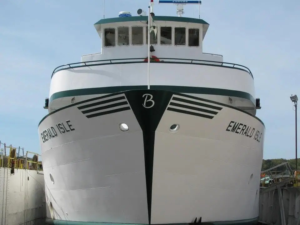 Front view of a white ferry with green trim, docked between waterfront structures.