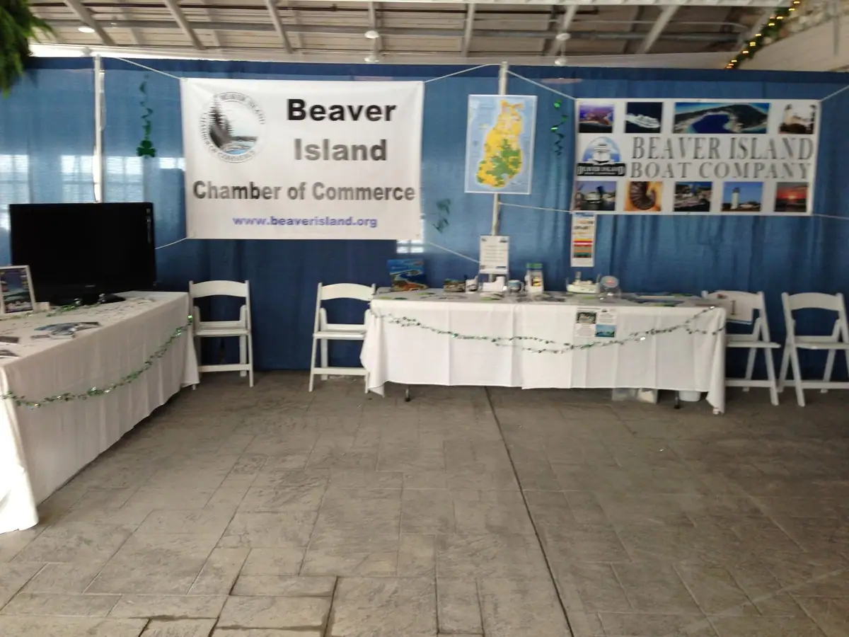 Indoor exhibition booth with draped tables, display banners, brochures, chairs, and a wall map.