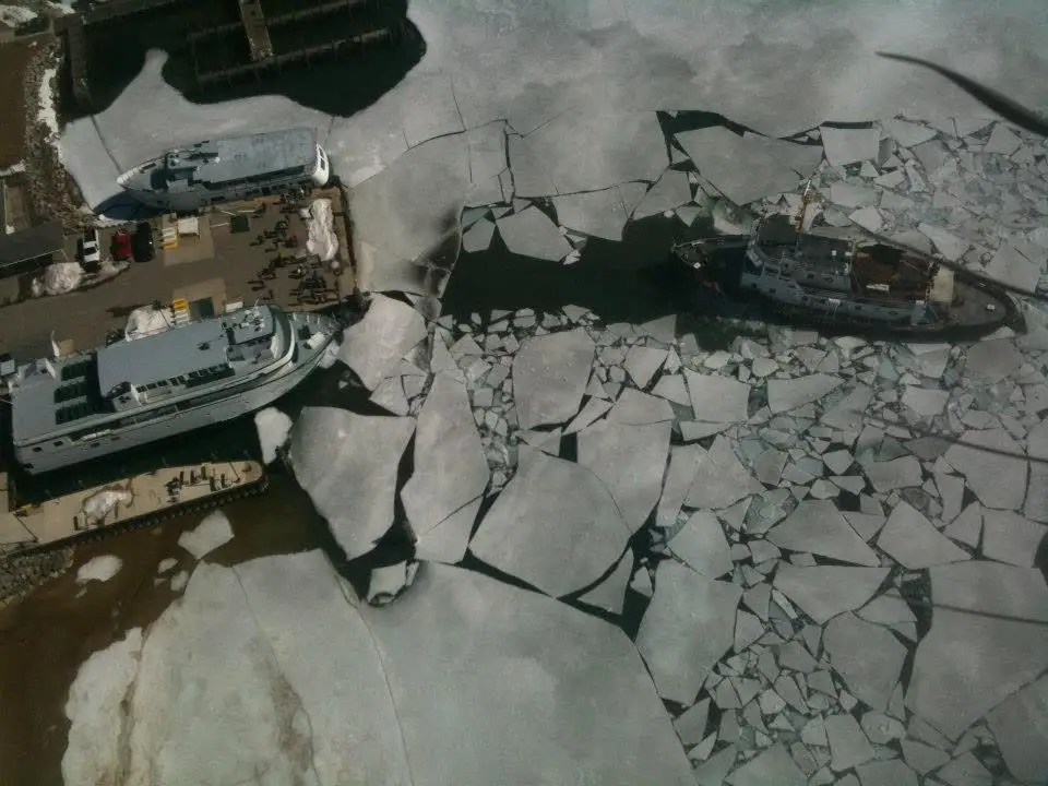 Aerial view of two passenger ferries and a workboat amid broken ice at a dock.