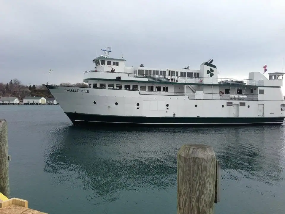 White passenger ferry with green trim moored beside a pier, with shoreline buildings in the background.