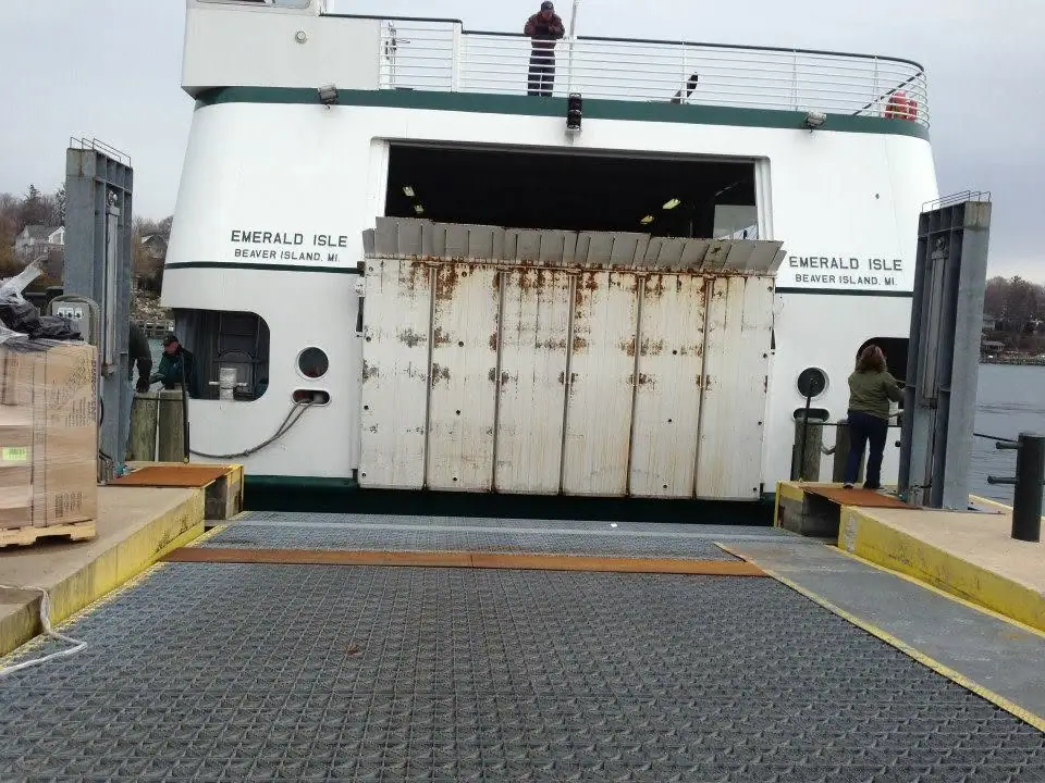 A ferry faces a loading ramp with its stern door open and people on the decks and dock.