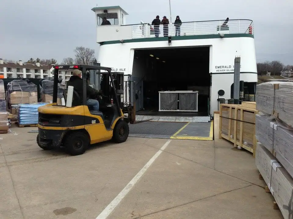 A forklift stands before a white ferry as cargo is prepared for unloading at a loading ramp.