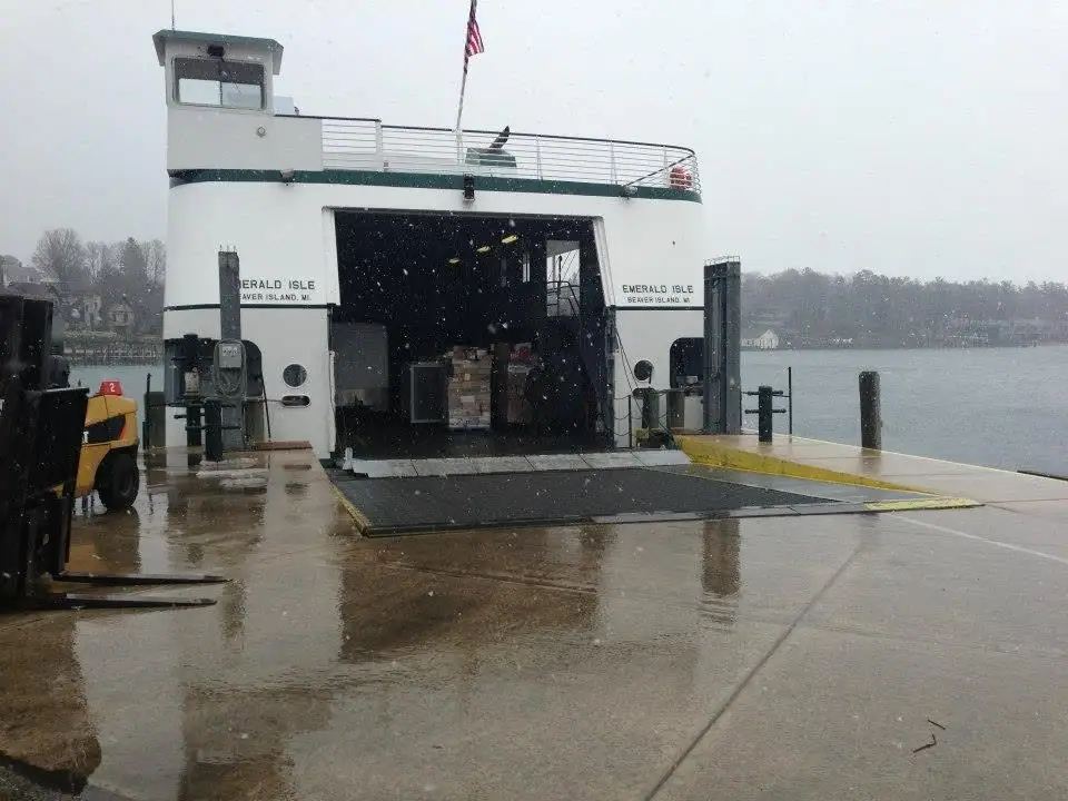 A white ferry with an open loading bay stands at a wet pier during snowfall.