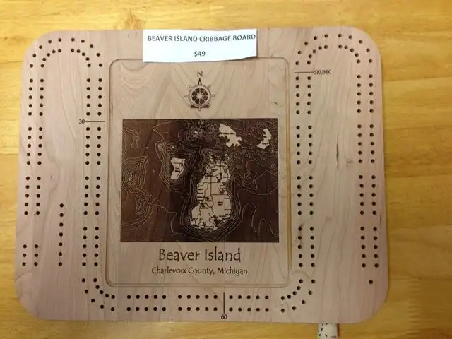A wooden cribbage board with peg tracks, a compass rose, and a printed map panel.