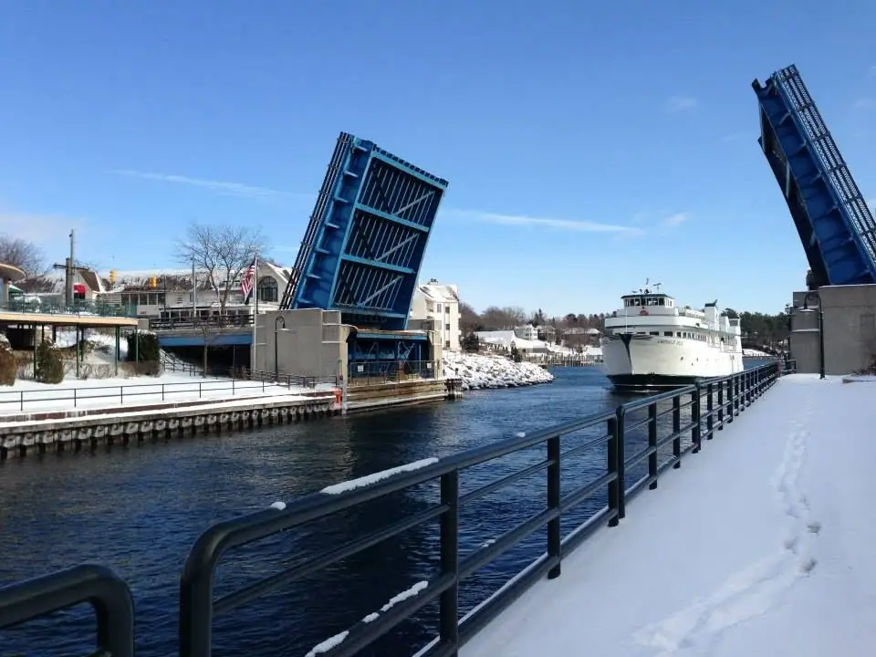 White ferry passing between raised blue drawbridge leaves in a snowy waterfront channel.
