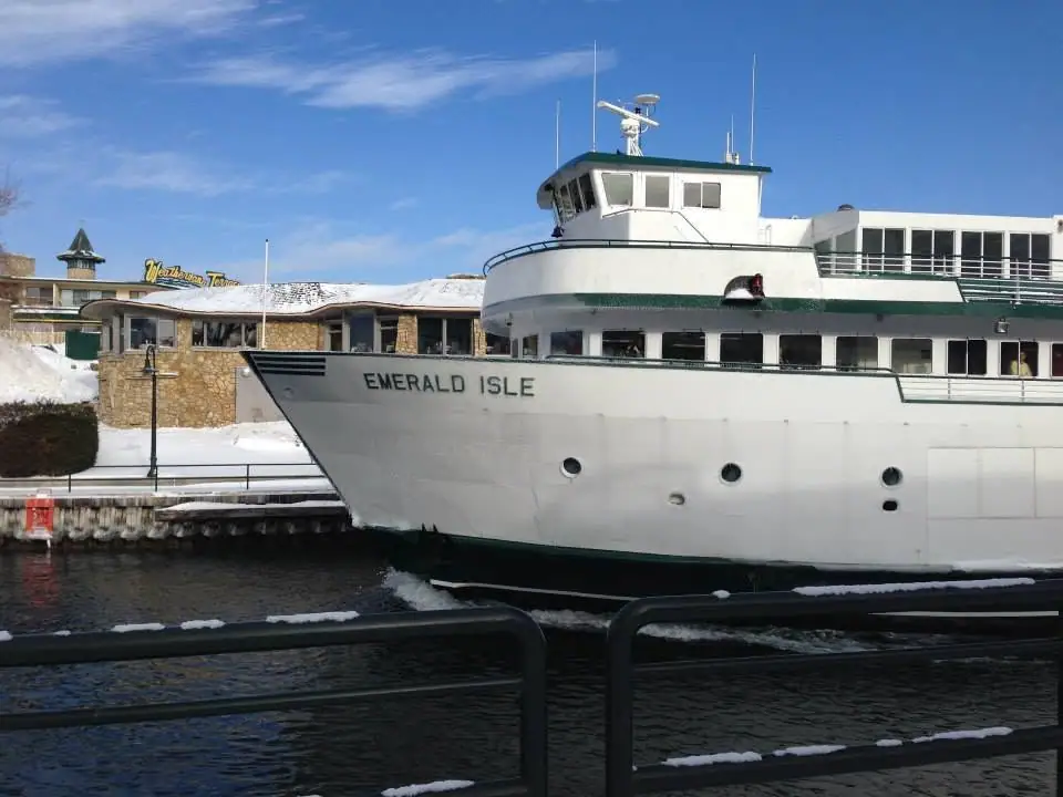 A white ferry named EMERALD ISLE is moored beside a snowy waterfront and a stone-faced building.