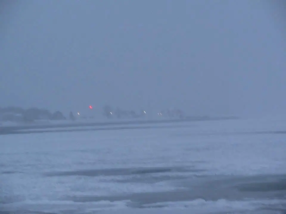 A blurred blue-gray winter scene with snow or ice in the foreground and distant lights beyond.
