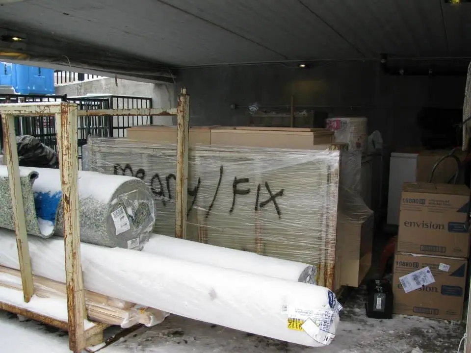 Wrapped rolls of material and cardboard boxes sit on a rusted rack in a dim, snow-covered storage area.