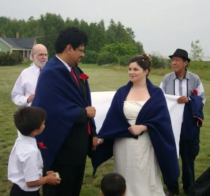 A bride and groom stand with attendants and children during an outdoor wedding ceremony.