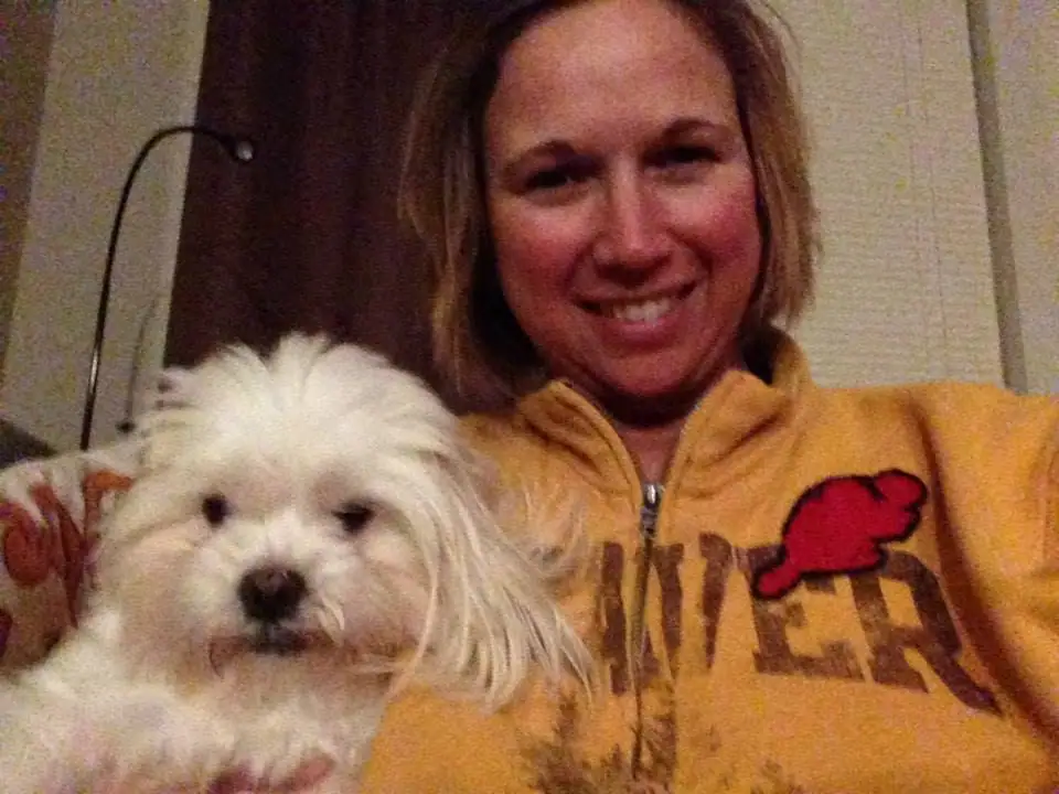 A smiling woman holds a small white dog in an indoor portrait.