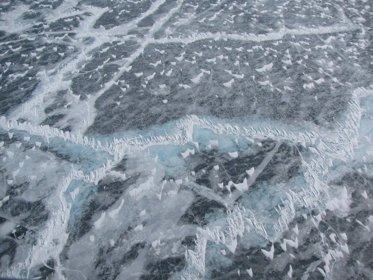Close view of gray-blue ice covered with white frost ridges and fractured patterns.