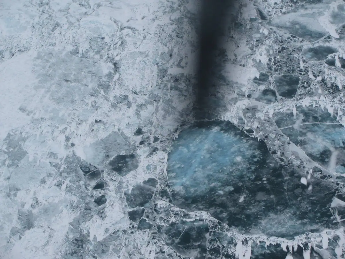 Aerial view of fractured white and blue ice surrounding dark openings and a long shadowlike area.