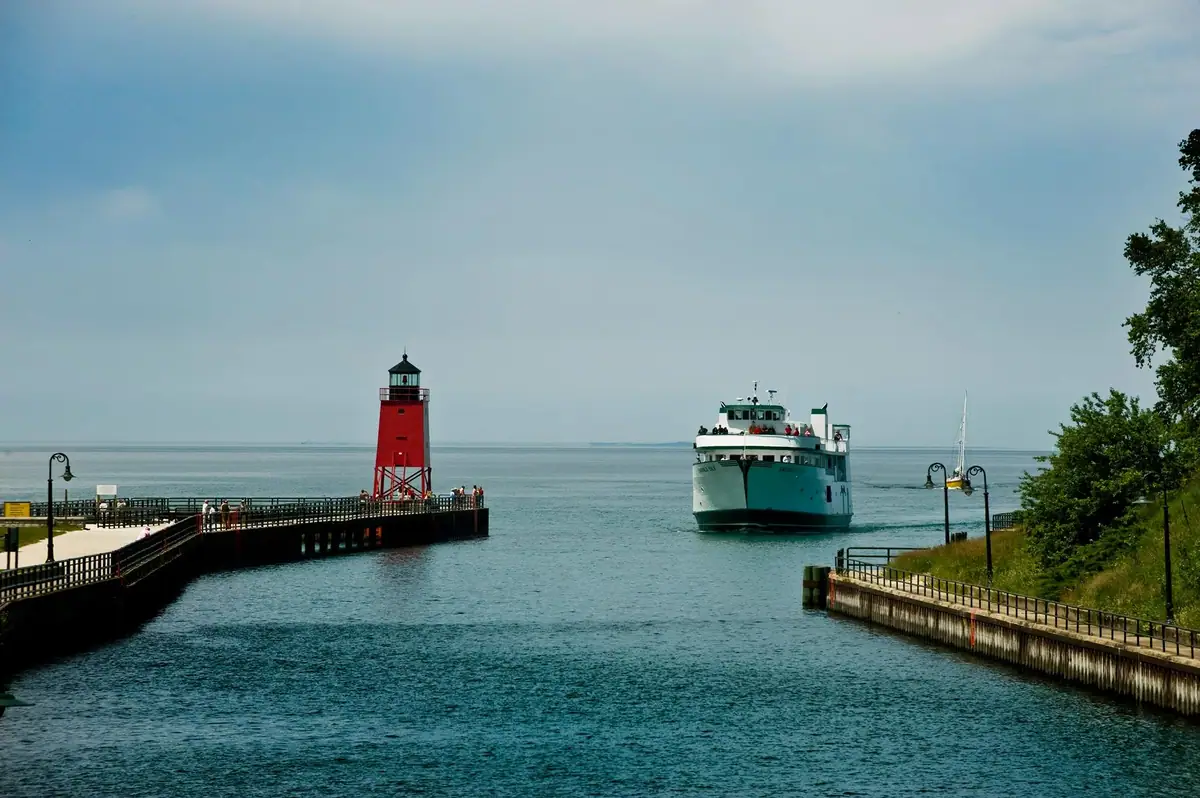 A passenger ferry approaches a channel beside a red lighthouse on a pier.