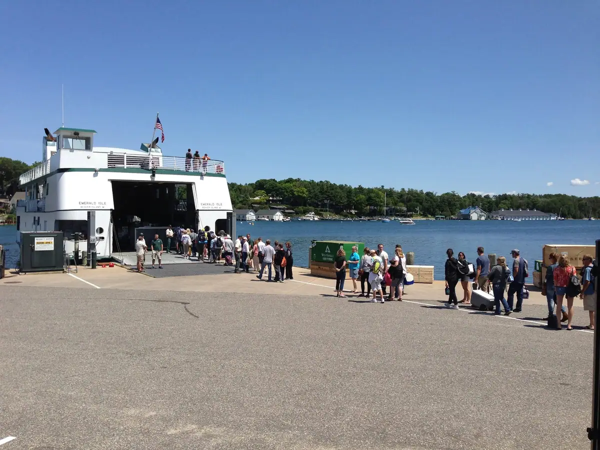A white passenger ferry loads and unloads travelers at a concrete pier beside a wooded shoreline.