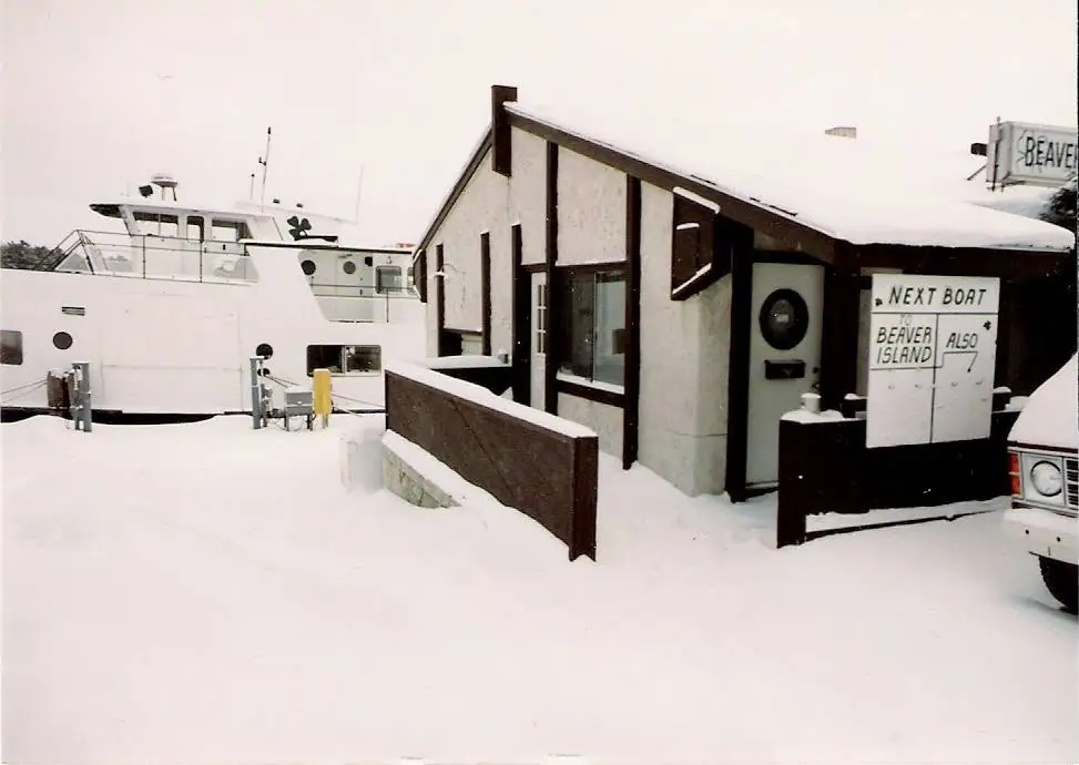 A white ferry and a small snow-covered terminal building stand beside signs in a winter scene.