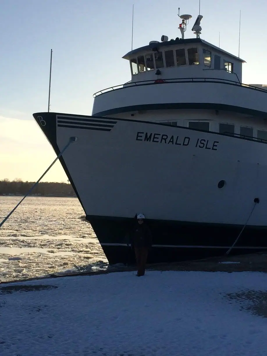 Large white ferry beside ice-covered water, with a bundled person standing on the snowy shore.